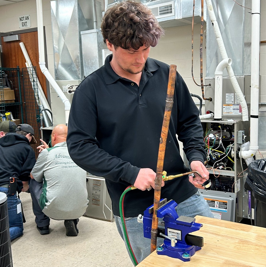 An HVACR student practices pipe brazing with a torch at a workbench vise.
