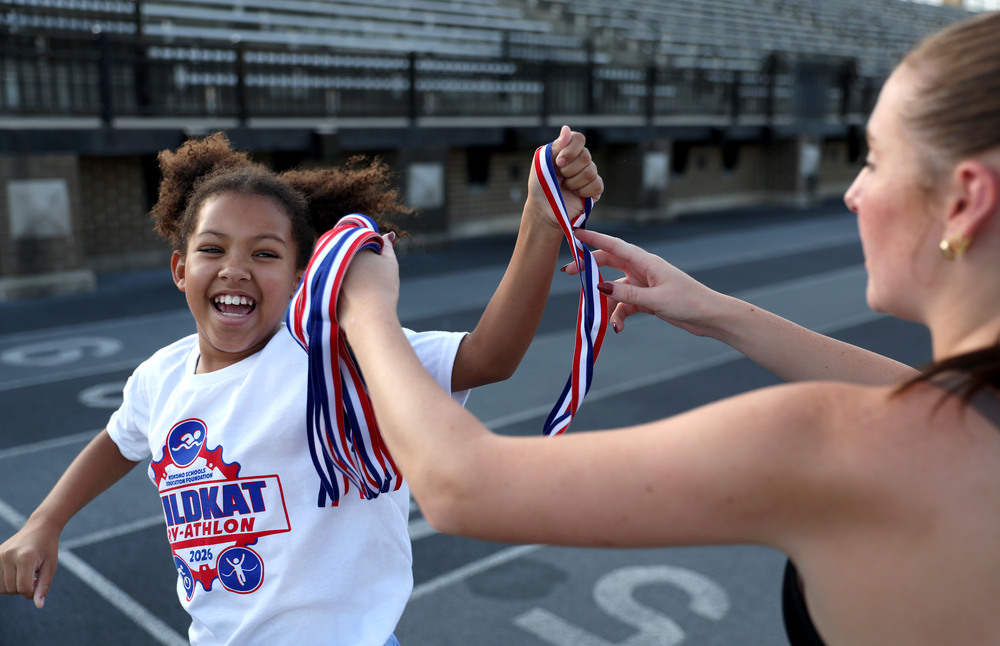 elementary age student athlete receiving medal as she crosses the finish line