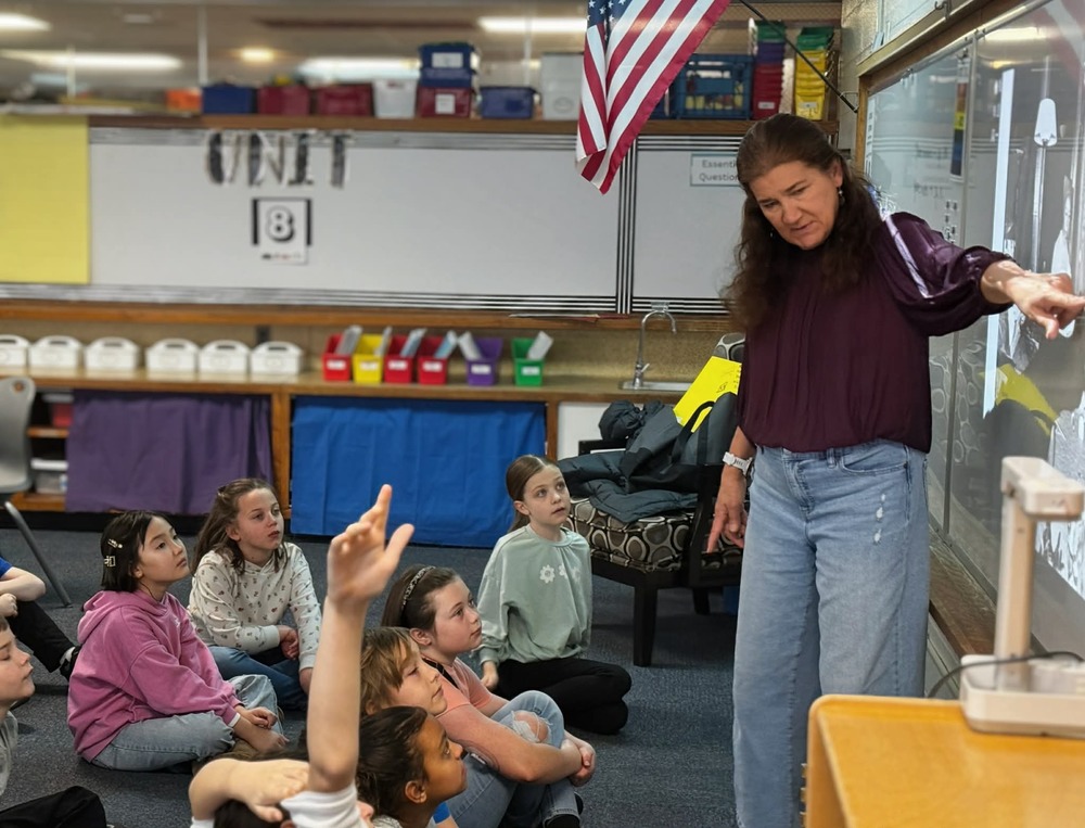 teacher pointing to white board and students participating in discussion