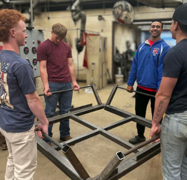 four male welding students holding platform