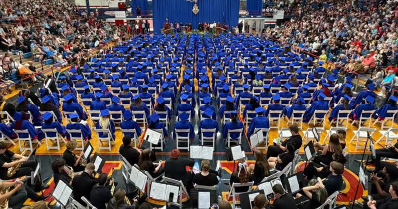 gymnasium full of graduates in caps and gowns and crowd to support them