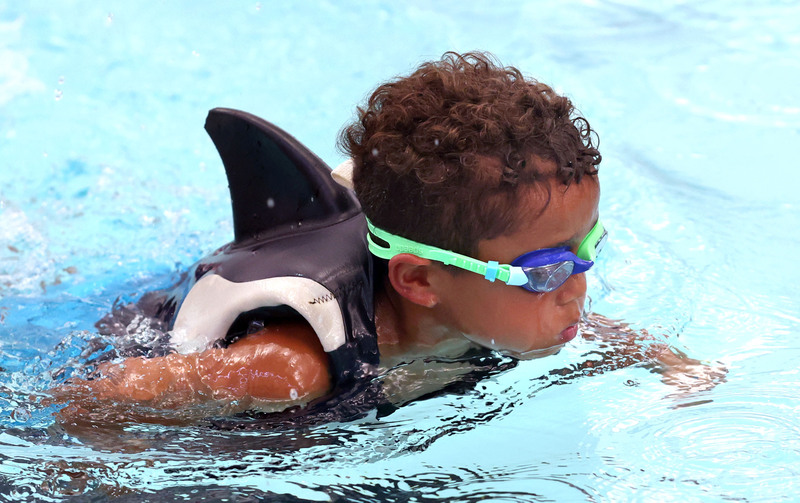 little boy swimming with goggles and shark fin life jacket