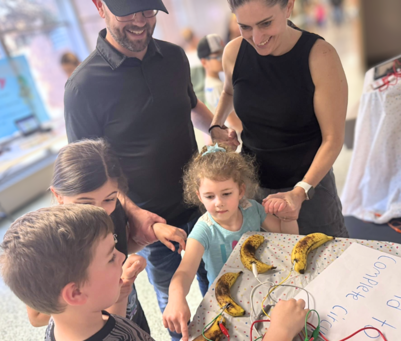 dad, mom, and three children all holding hands to complete a circuit and connect the dots