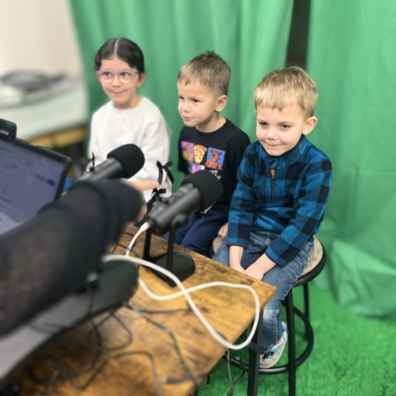 elementary students with microphones and green screen backdrop