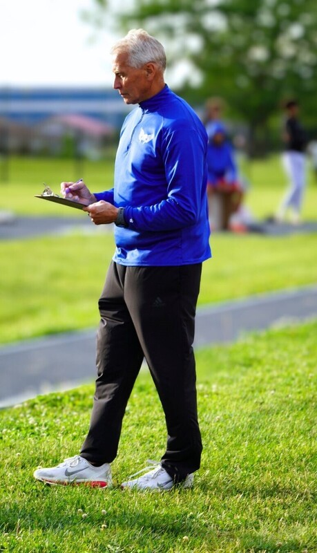 man standing in athletic gear holding clip board on track and field course
