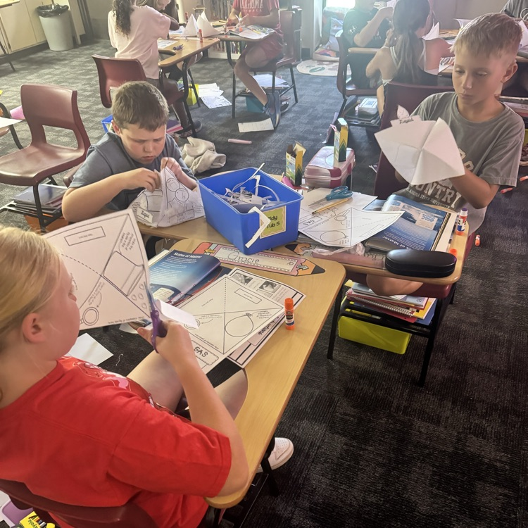 students cutting and glueing paper to form a states of matter pyramid