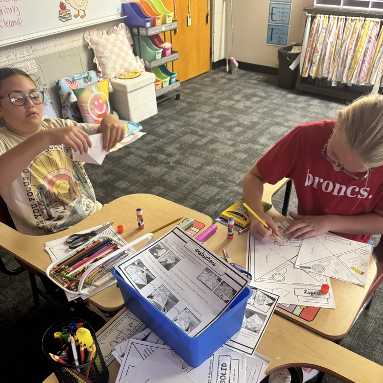 students cutting and glueing paper to form a states of matter pyramid