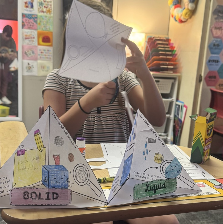 students cutting and glueing paper to form a states of matter pyramid