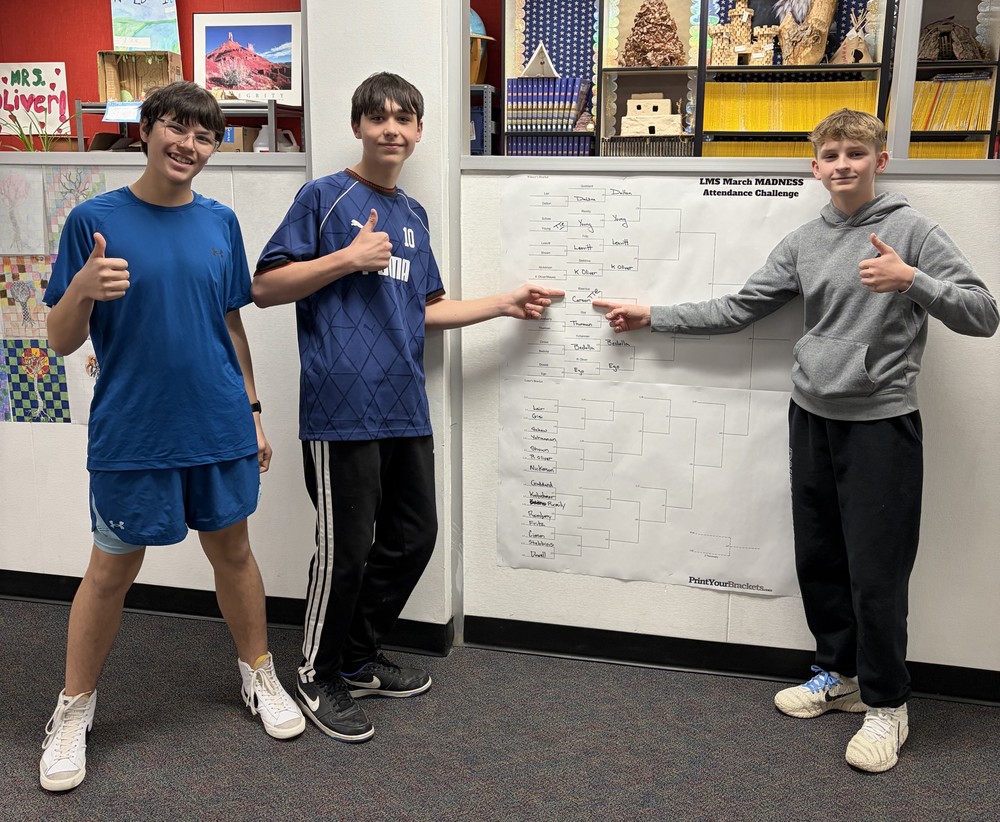 photo of three LMS students infront of the march Madness attendance challenge brackets
