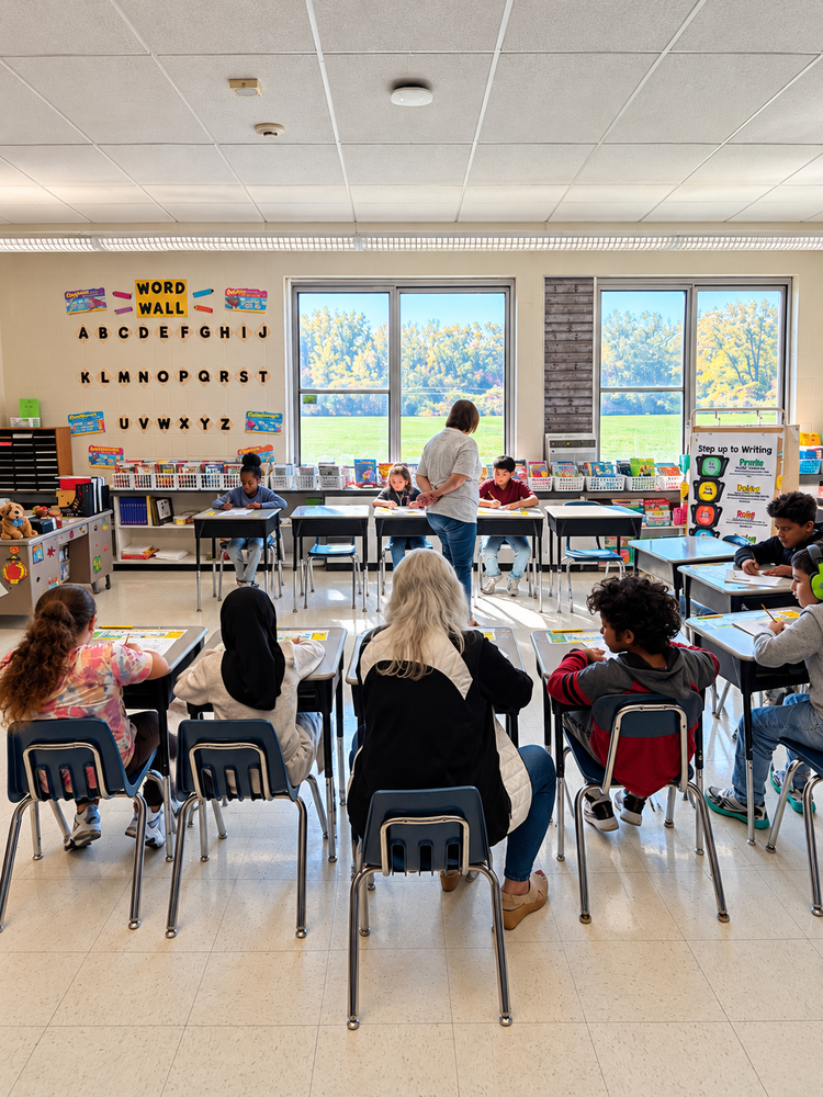 students in circle at desks with teacher walking in middle