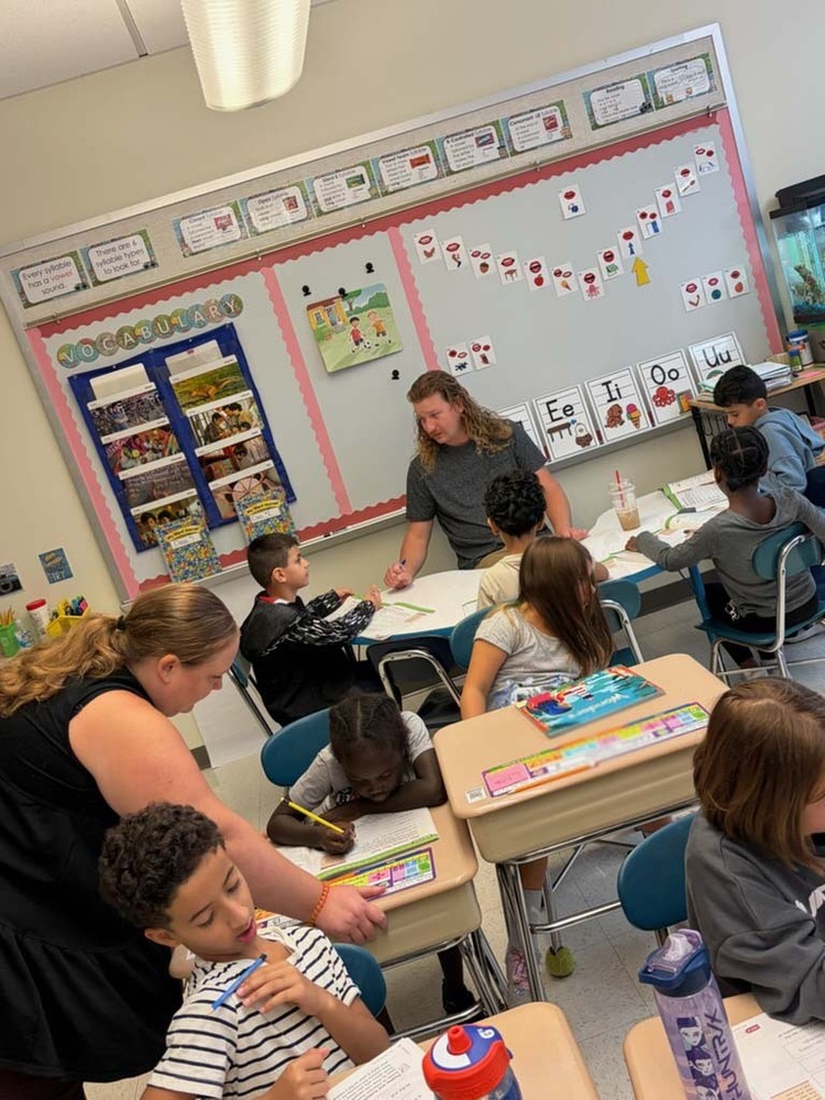students at desk with teachers walking around helping