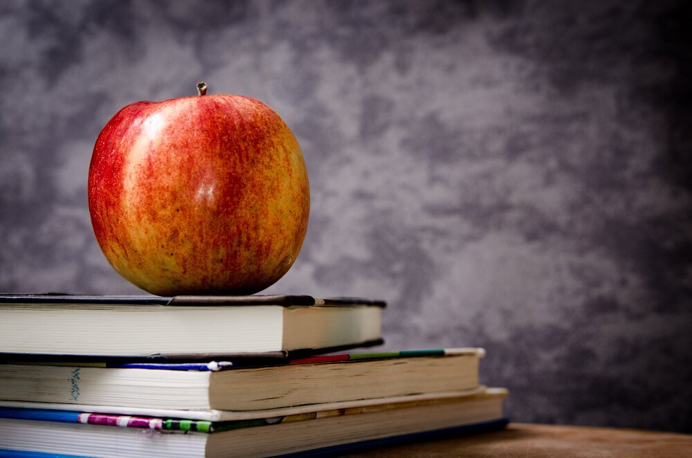apple on stack of books with chalkboard in background
