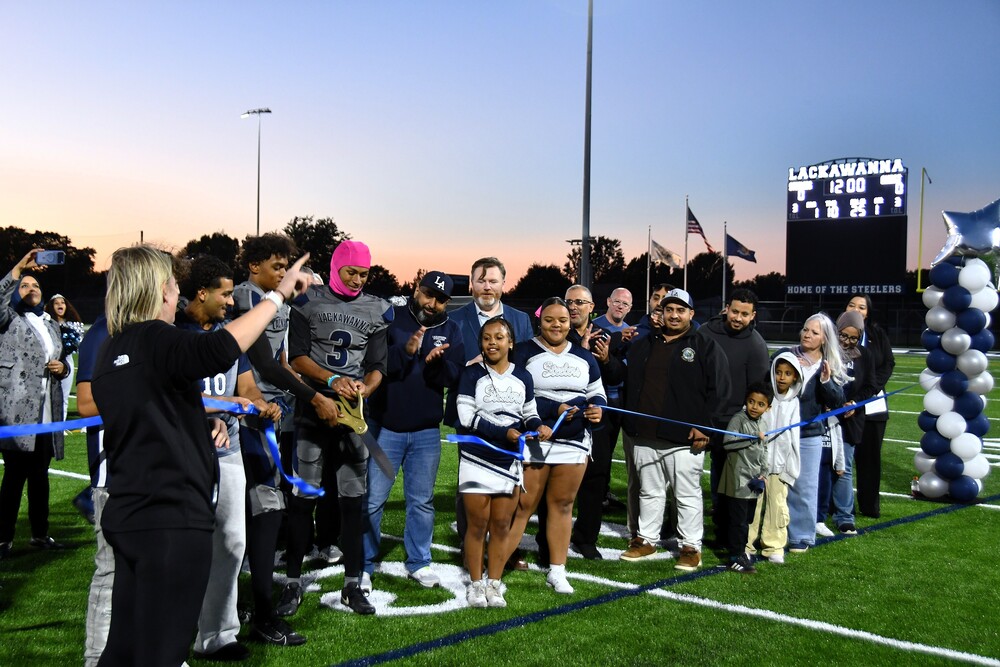 student athletes, coaches and school leaders line up on football field to cut ribbon