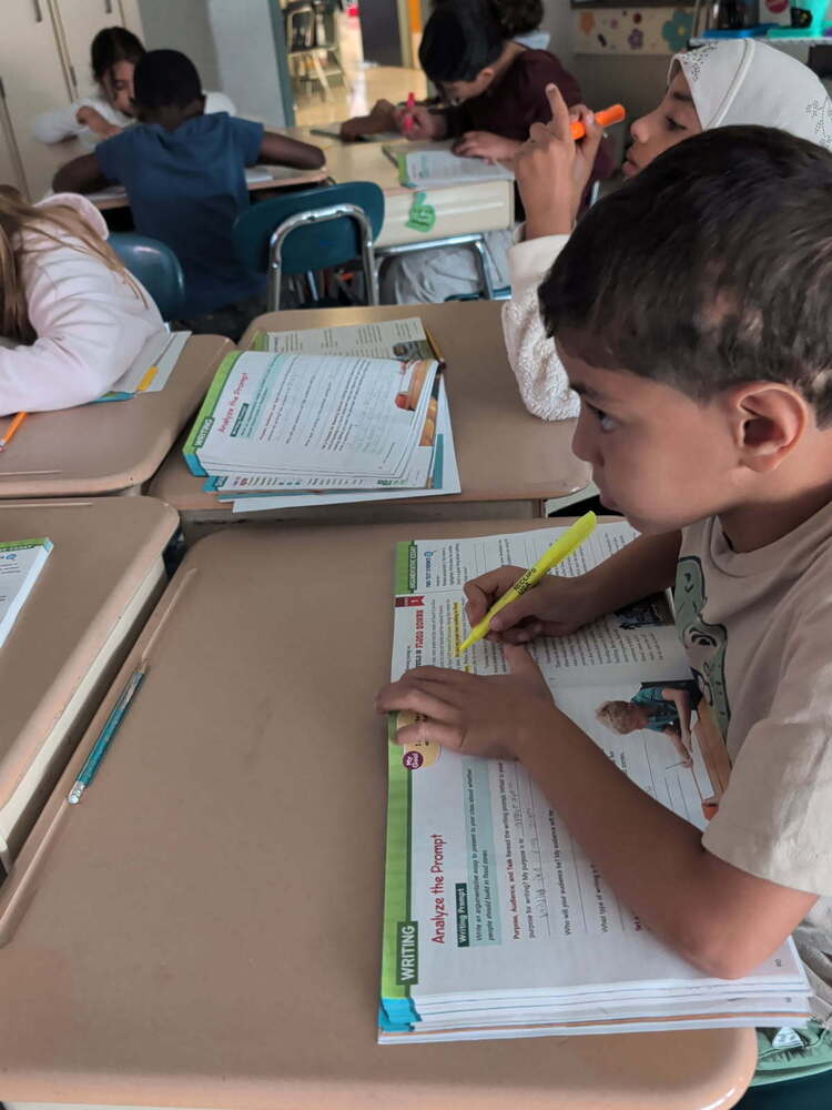 student works at desk with workbook in front of him