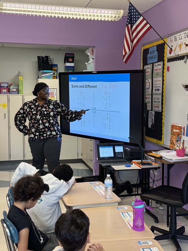 teacher stands in front of class pointing at smart board