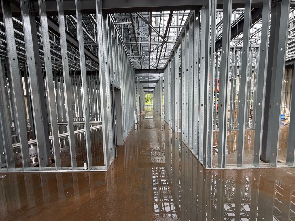 Alt text: An interior view looking down a long, central hallway framed with closely spaced, vertical light-gauge metal studs. 