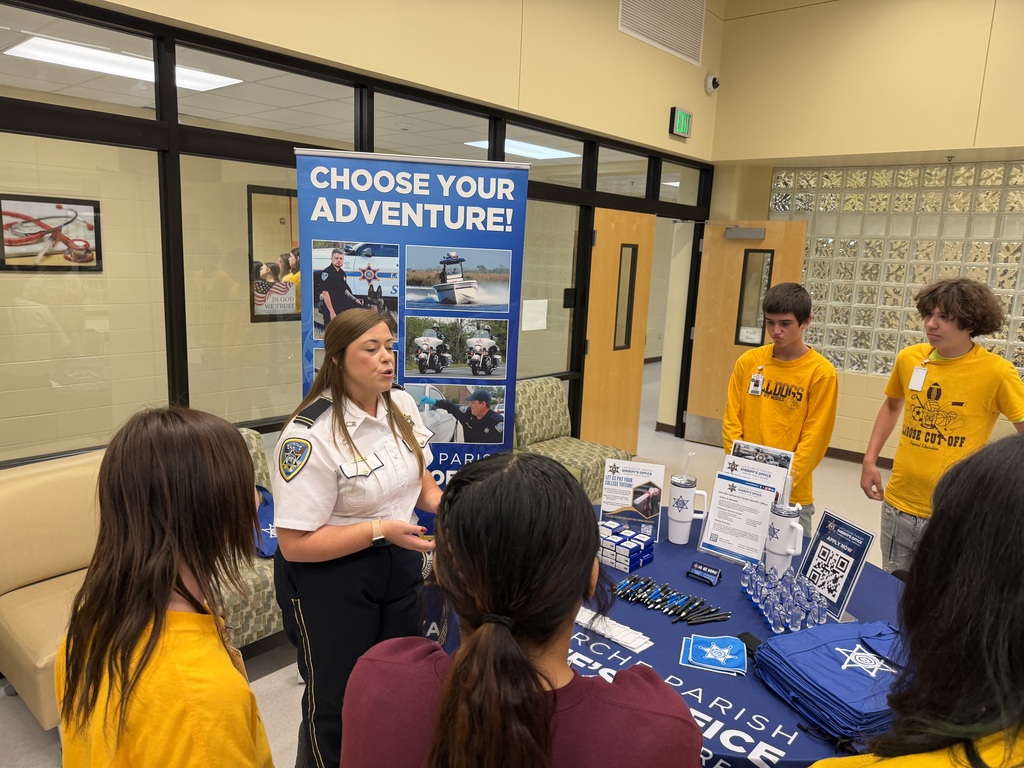 A police officer in uniform speaks to a group of students gathered around a table.