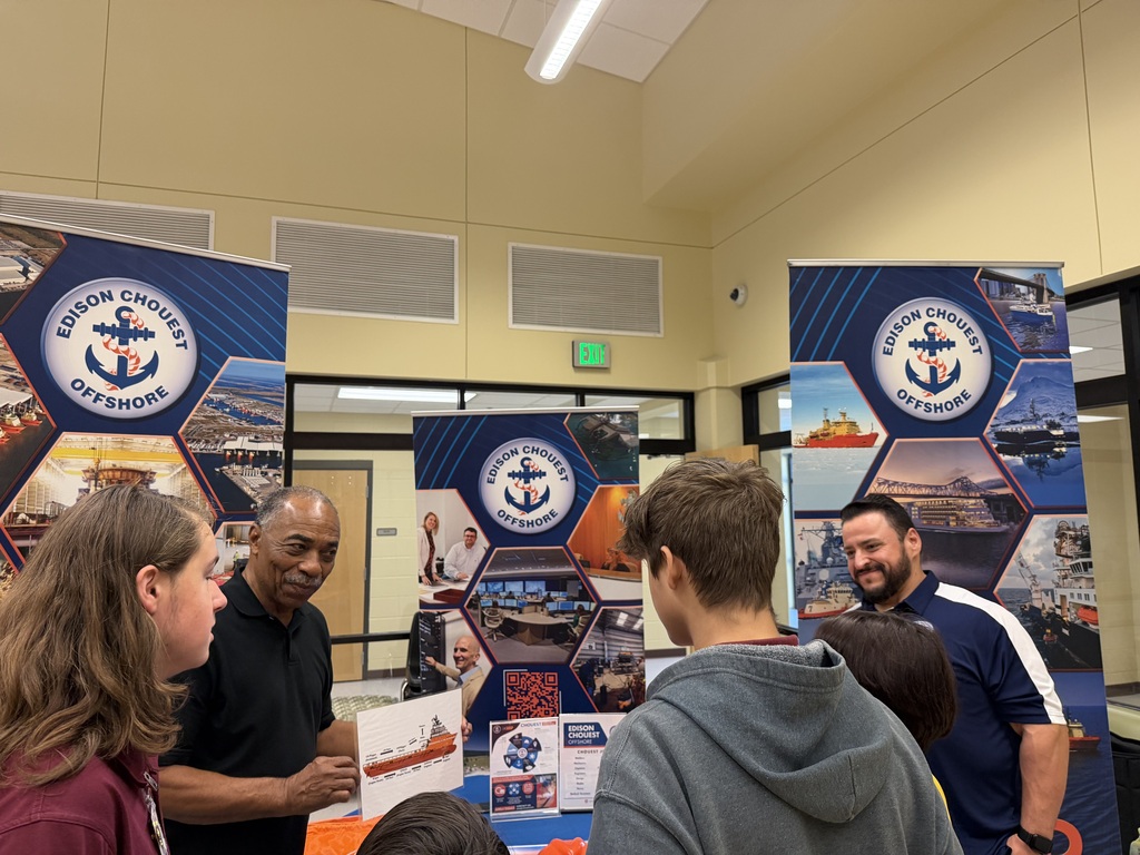 People are gathered around a table displaying information at an event. Three banners are visible, two with a blue background and the third a light blue.