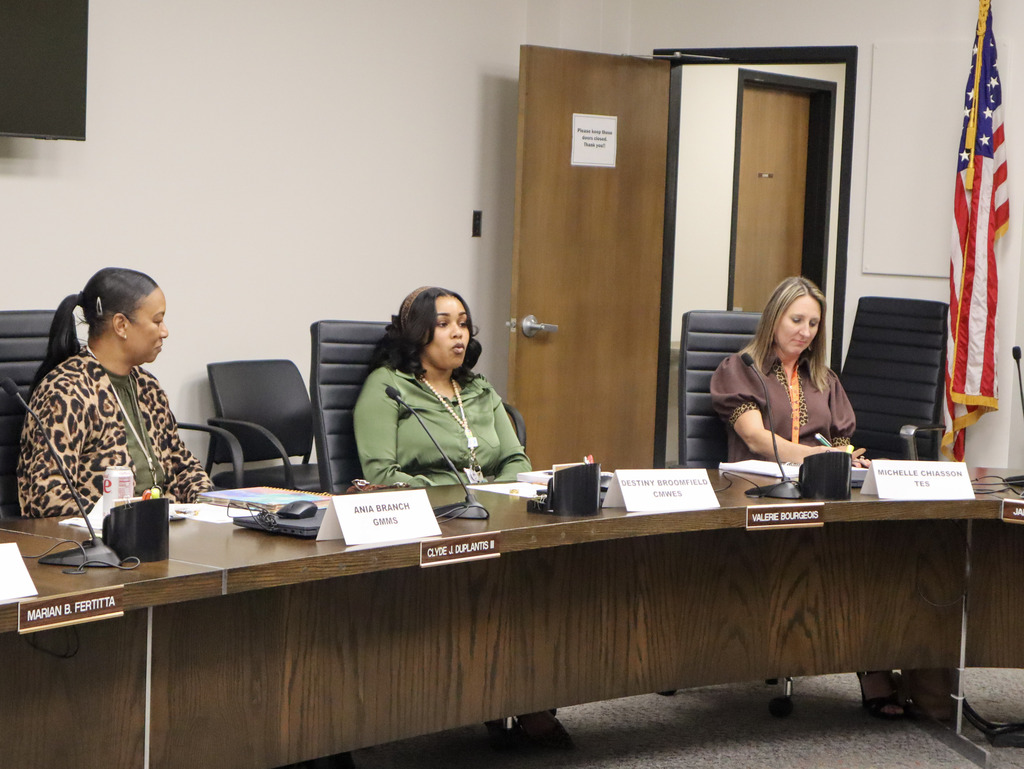Four women seated at a table with name cards, microphones, and open doors behind them.