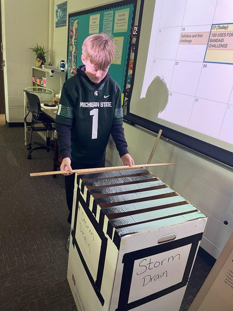 Student in STEM class helping to get keys out of a faux storm drain