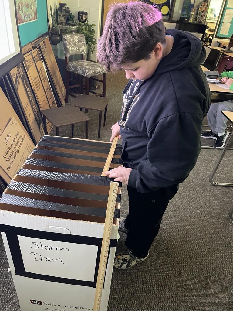Student in STEM class helping to get keys out of a faux storm drain