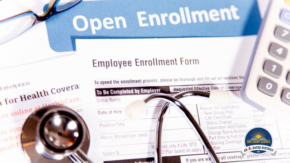 Scattered paperwork that says "Open Enrollment," Employee Enrollment Form,: and "Health Coverage." A stethoscope, pair of eyeglasses and a calculator are on top of the papers, and the Lake County Schools logo is in the bottom right corner