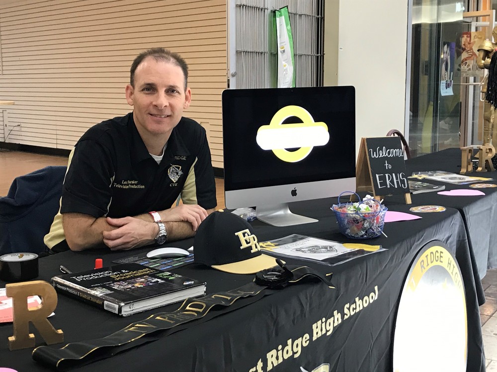 William Lee Fouraker sitting at table with East Ridge High School tablecloth, yearbook, hat and logo on it.