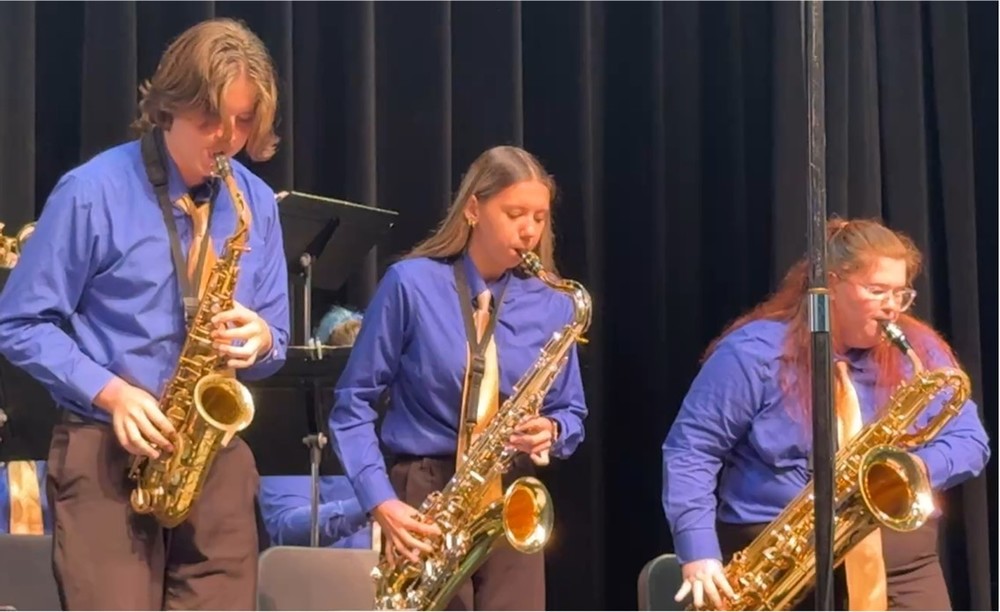 One teen boy and two teen girls all playing saxophones 
