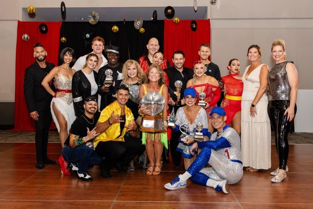 Group of dancers in performance costumes with Dr. Stephanie Luke in the center holding the mirror ball trophy
