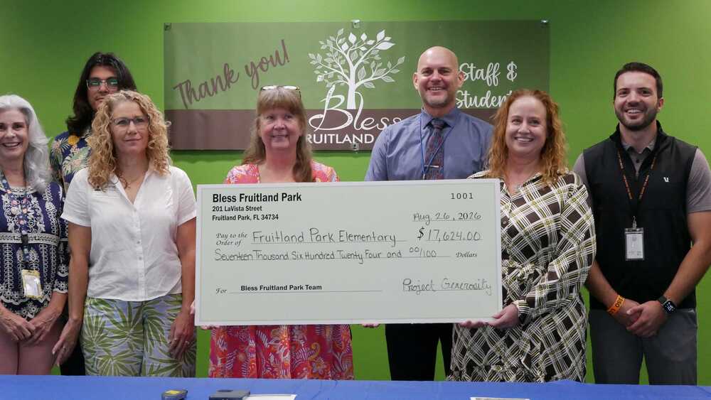 Group of adults holding large display check made out to Fruitland Park Elementary from Bless Fruitland Park for $17,624