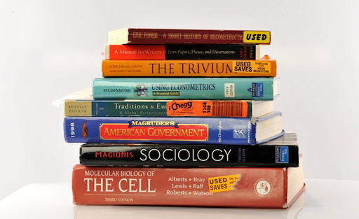 Stack of used text books on a table against a white background. 