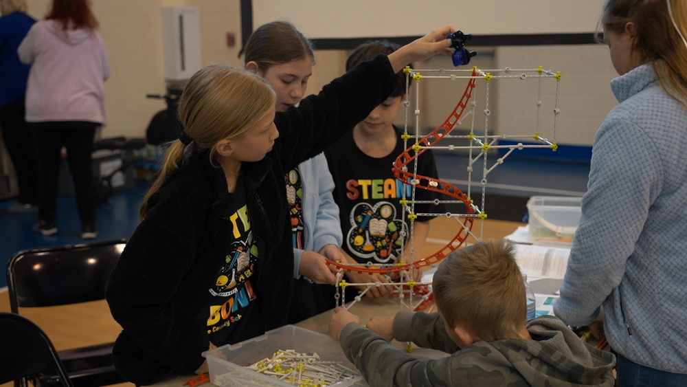 Students gathered around a table building a table-top roller coaster