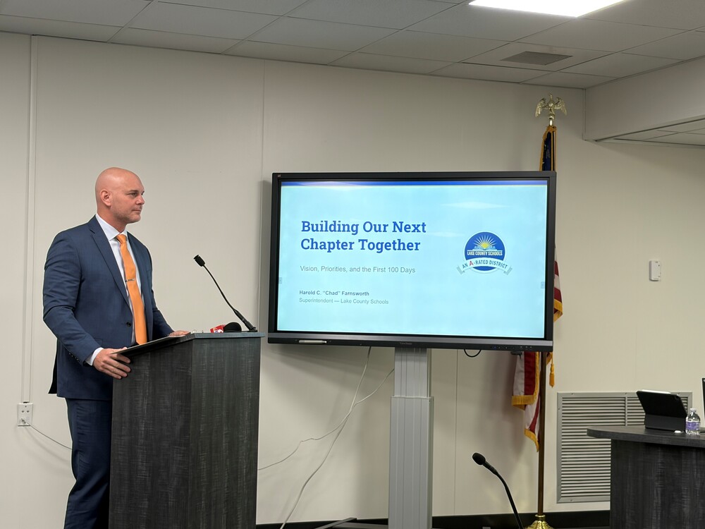 Chad Farnsworth at podium. Presentation screen shows a slide that reads, "Building Our Next Chapter Together."