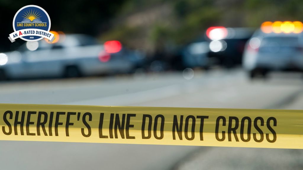 Blurred cop cars in the background with yellow tape in foregrond that reads, "Sheriff's Line Do Not Cross."