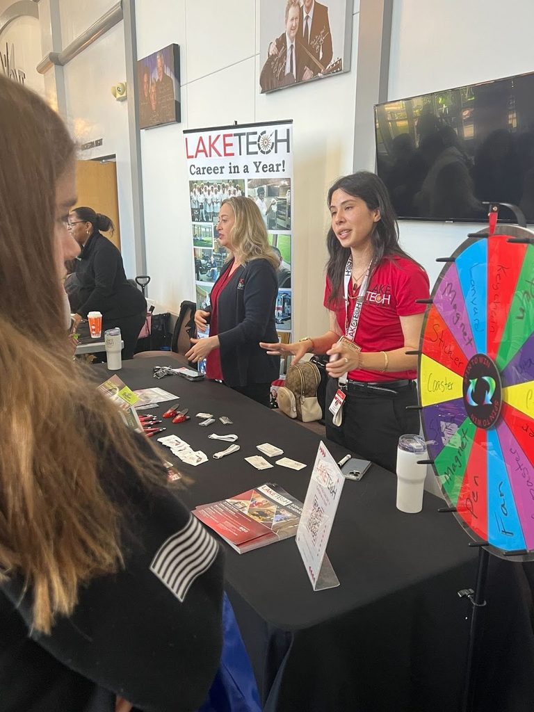 Vendors behind table with a Lake Tech banner in the background talking with a student.