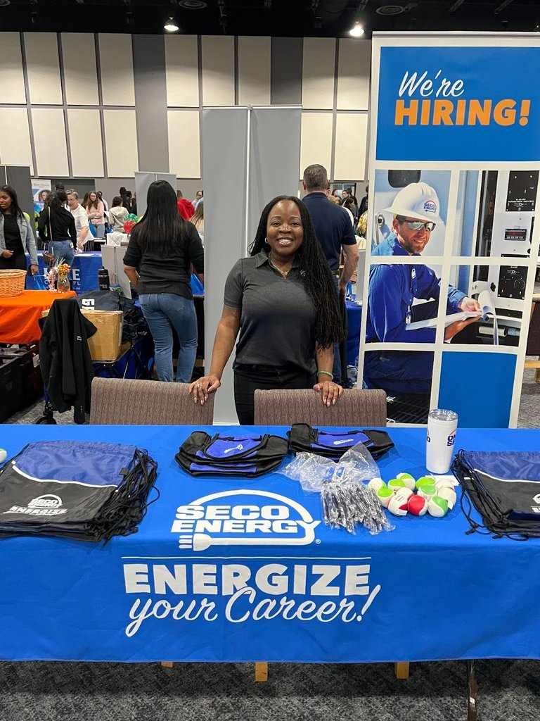 Female vendor smiling behind a table with a blue tablecloth that says SECO Energy, Energize Your Career. 