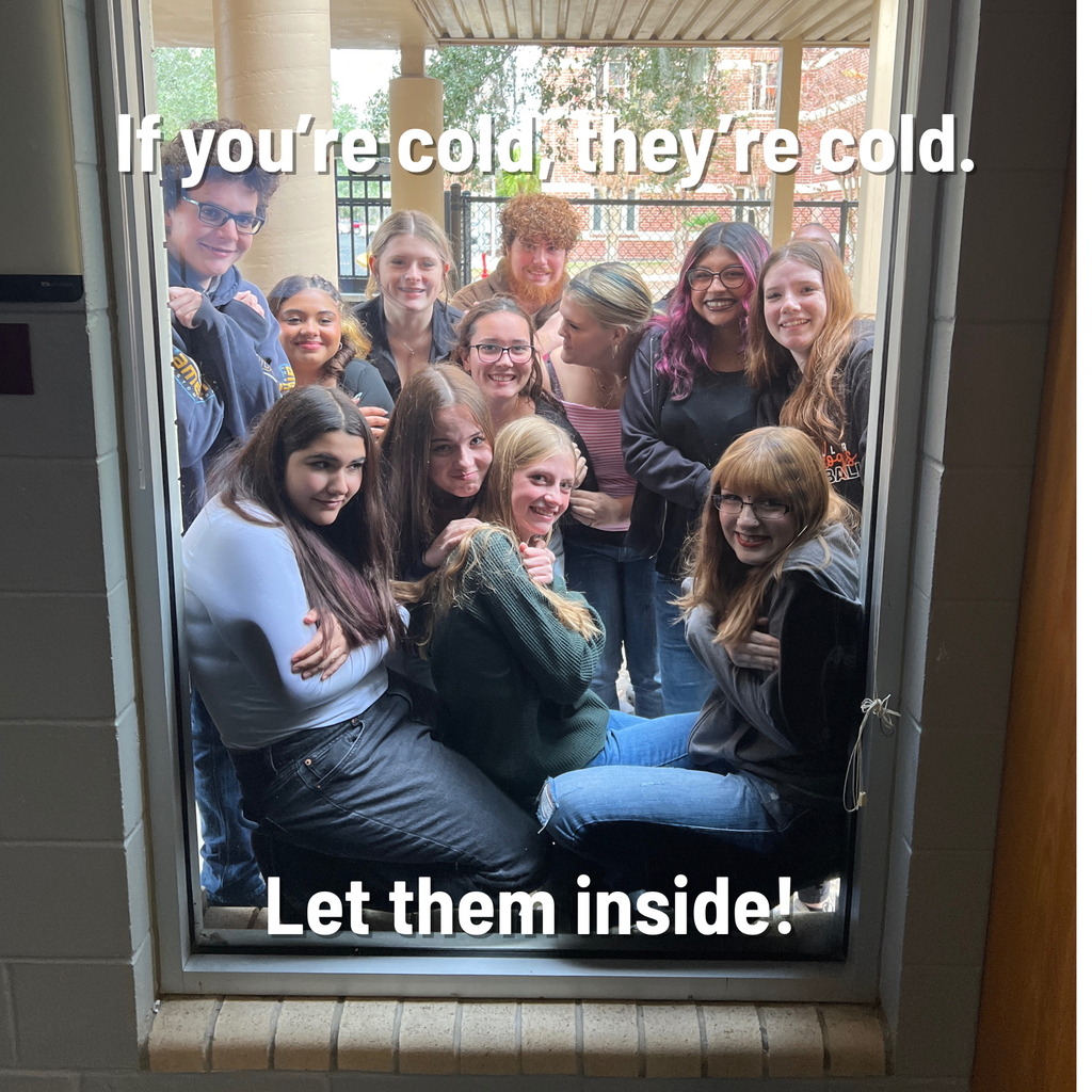 Students huddle outside of a window looking in.