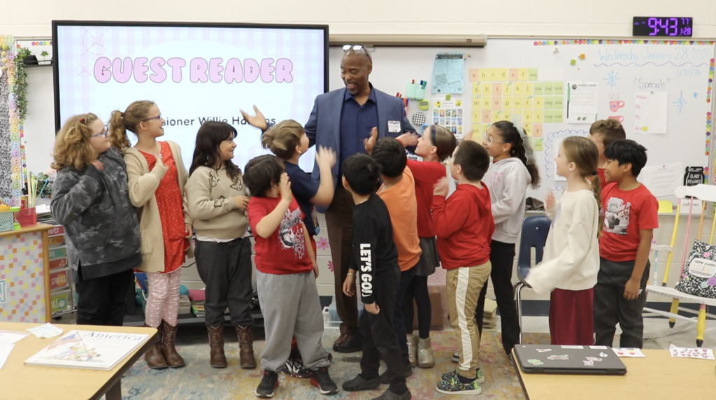 Students standing around Eustis mayor with sign in background that says "Guest Reader."