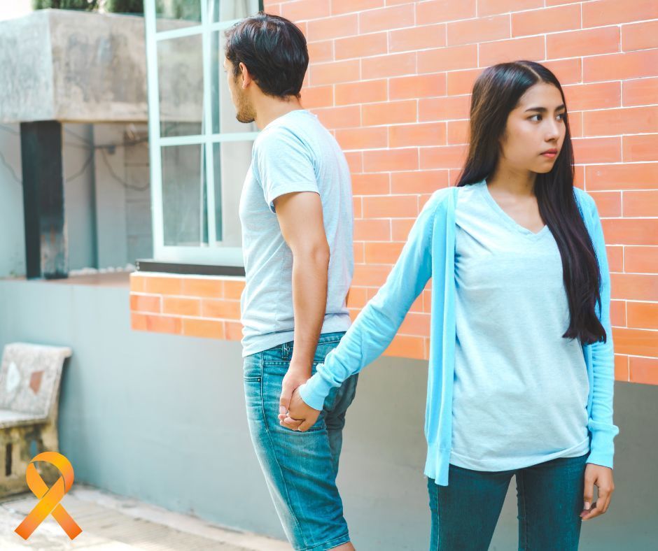 Teen boy and girl holding hands and pulling away, back to back, in opposite directions. Orange ribbon in bottom left corner.