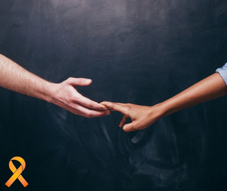 Male and female hands touching at the fingertip, as if almost holding hands. Orange ribbon in bottom left corner. 