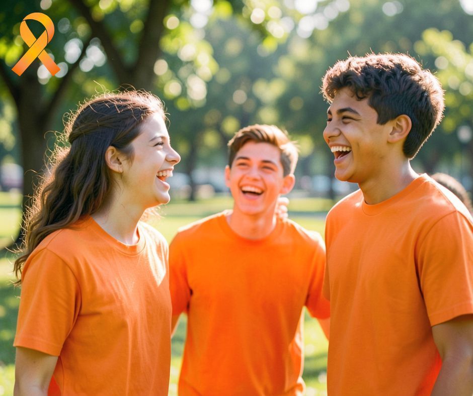 Teen girl laughing with two teen boys, all three wearing orange T-shirts
