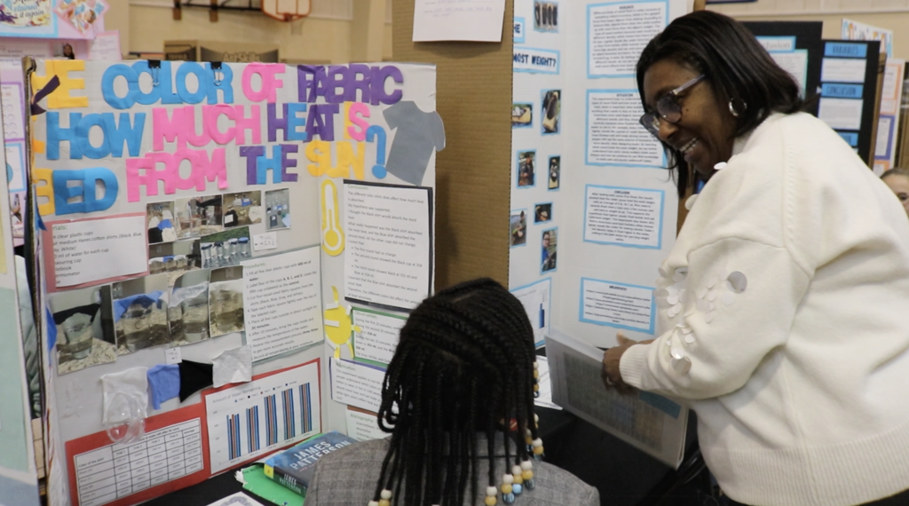 Board member Molly Cunningham talks with girl about her project in front of display board. 