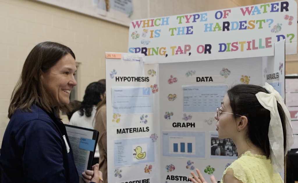 Judge talks to female student about her project, "Which type of water is hardest - spring, tap or distilled?"