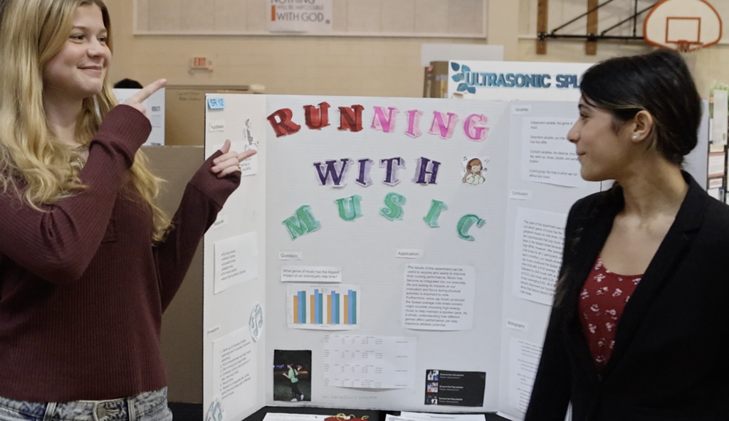 Two female students stand in front of project, "Running with Music"
