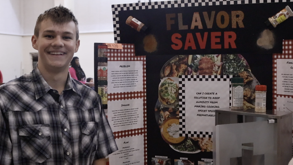 Male student stands and poses in front of his project, "Flavor Saver"