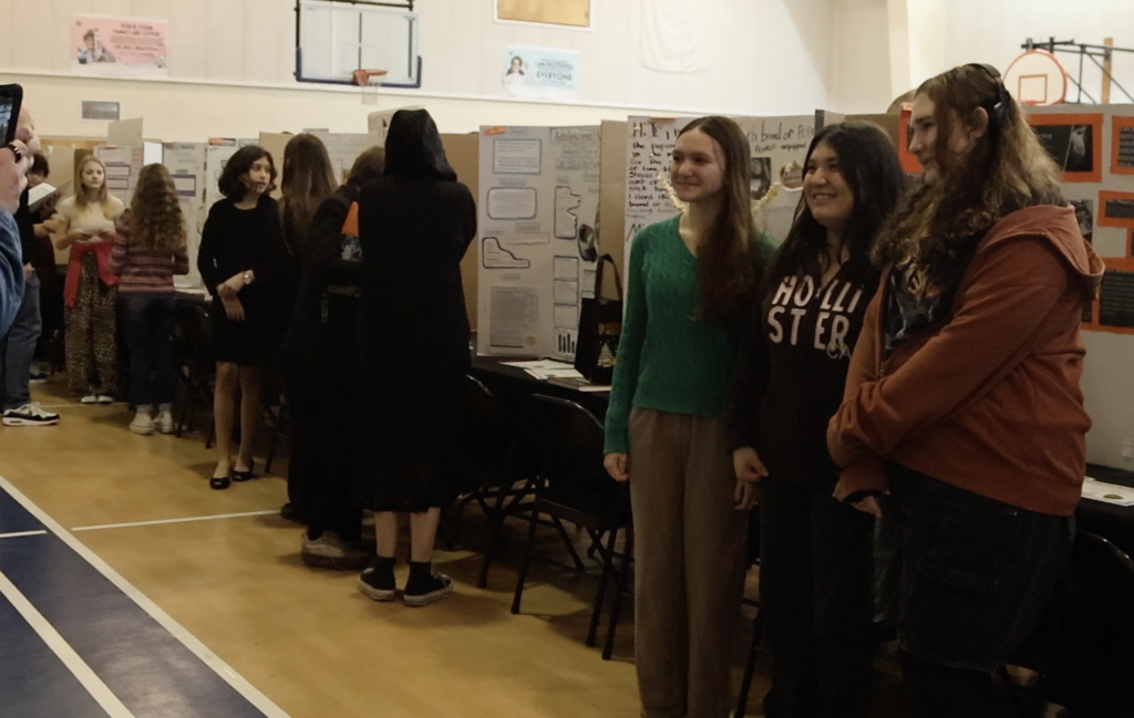 A row of projects with students standing in front of each of one. 