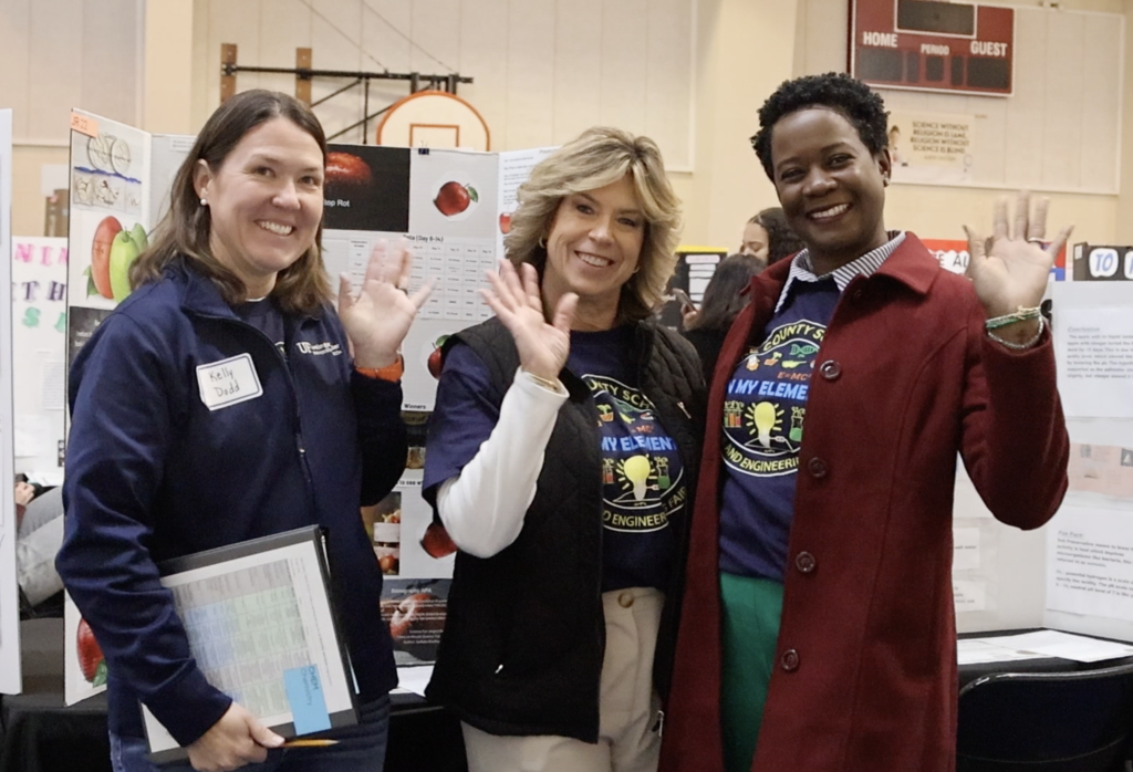 Three female judges pose and wave