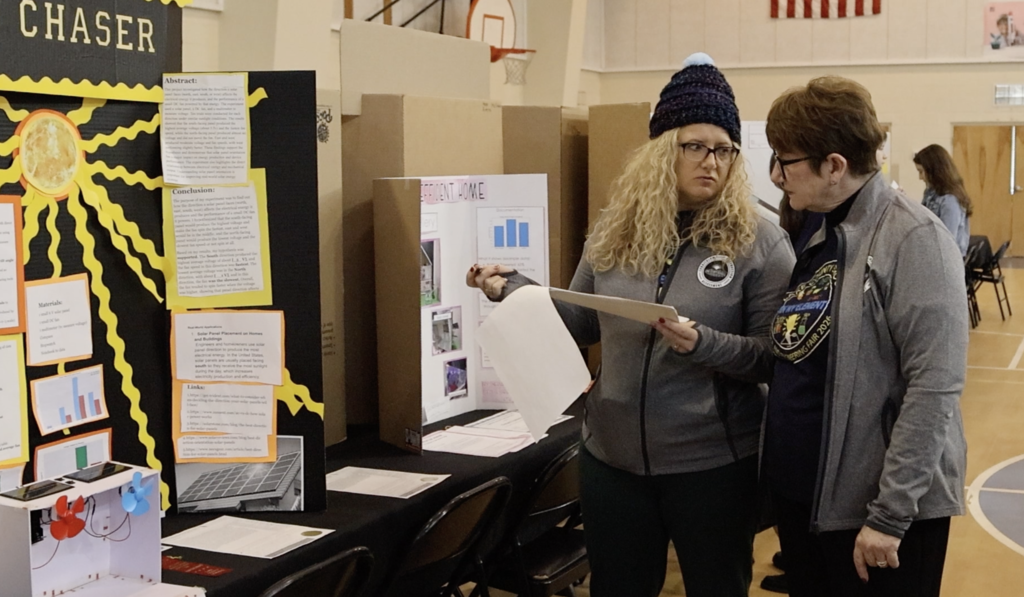Two female judges discuss a project, title is not clearly visible