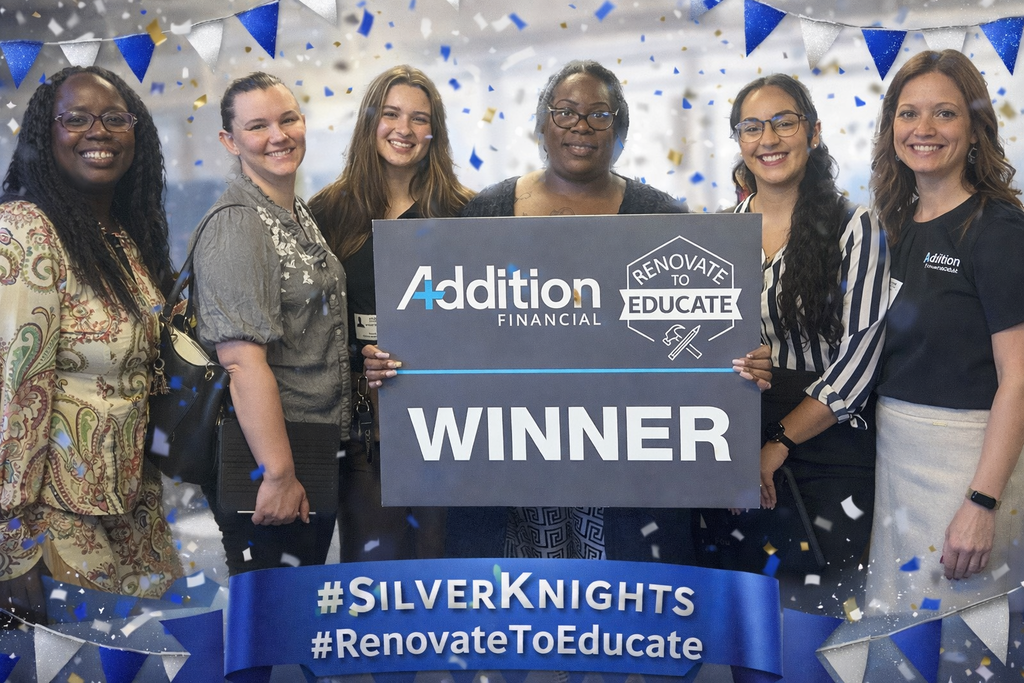 Six women stand together smiling and holding a large sign that reads “Addition Financial – Renovate to Educate – WINNER,” celebrating Oak Park Middle School being selected for a classroom makeover through the Addition Financial Renovate to Educate program.