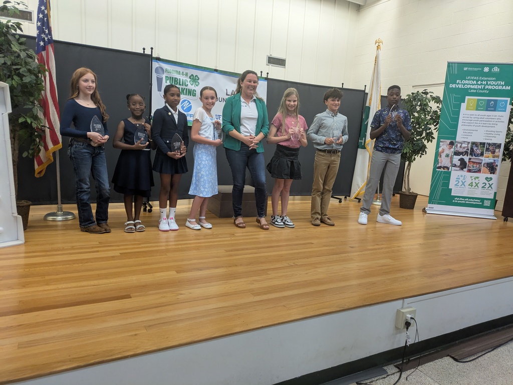 7 students on stage holding trophies, and a teacher standing in the middle